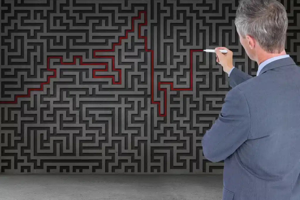 A man is standing with a marker in his hand next to a board with a maze drawn on it