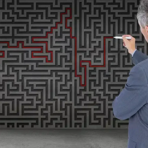 A man is standing with a marker in his hand next to a board with a maze drawn on it