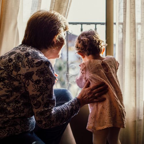 A grandmother with her grandson are standing on the windowsill looking at the street